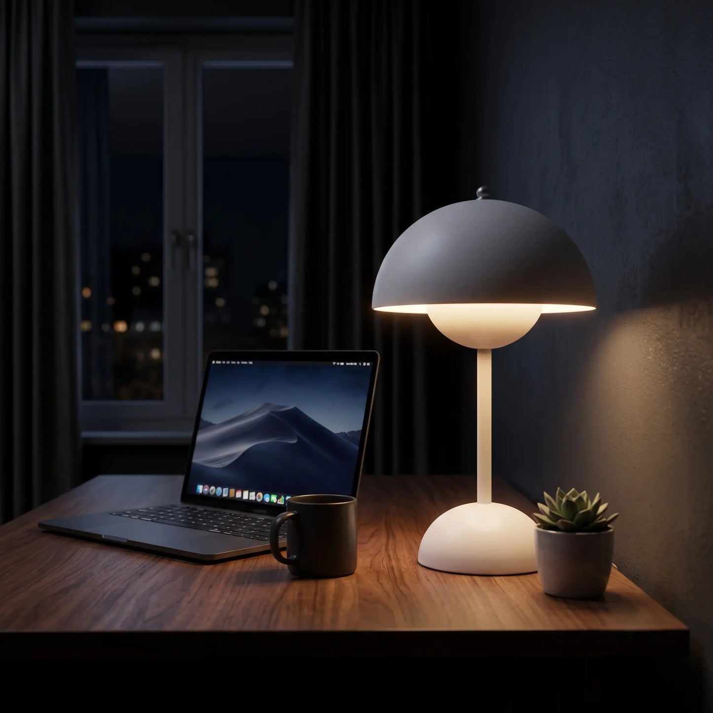 Aesthix Lume Bud white retro table lamp lit on a desk beside a laptop at night.