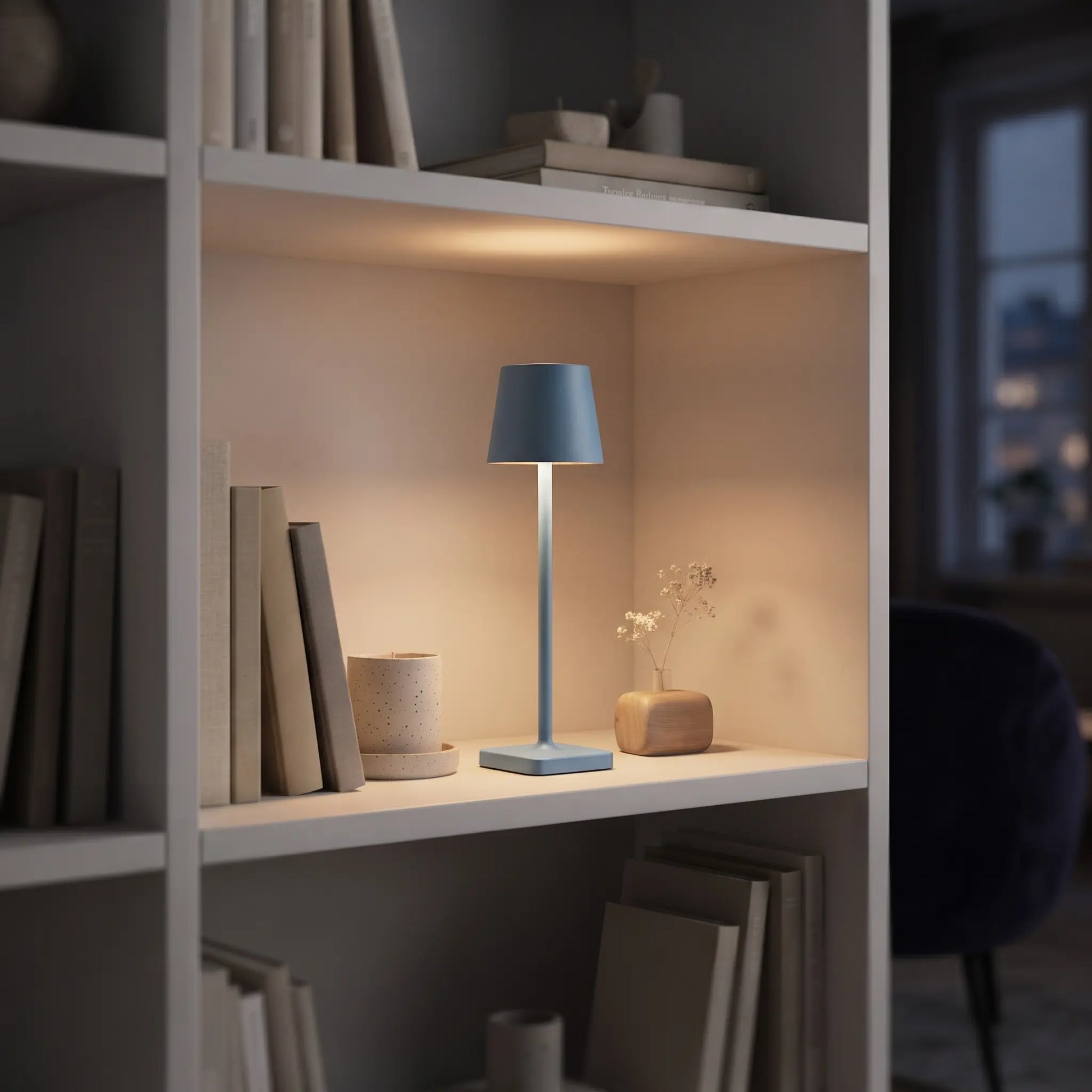 Aesthix Lume Classic blue bar style touch table lamp glowing on a styled bookshelf with books