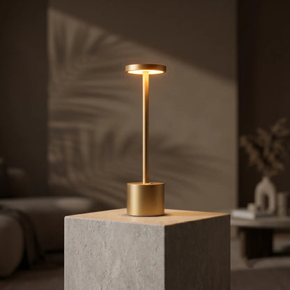 Aesthix Lume Halo gold cordless dimmable table lamp on a stone block with leaf shadow outdoors