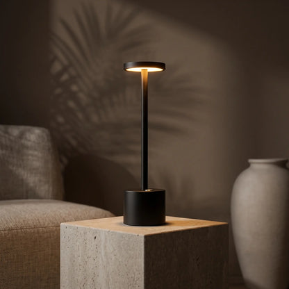 Aesthix Lume Halo black cordless dimmable table lamp glowing beside an armchair with a vase