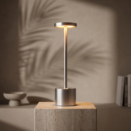 Aesthix Lume Halo silver cordless dimmable table lamp glowing against a wall with leaf shadow