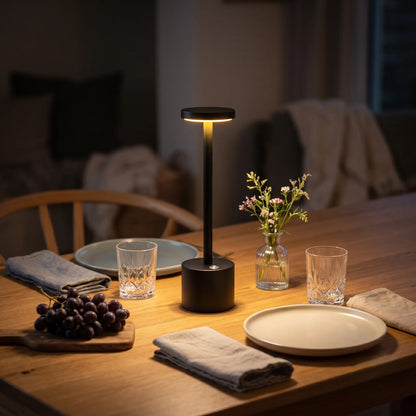 Aesthix Lume Halo black cordless dimmable table lamp on a wooden dining table with fruit and plates