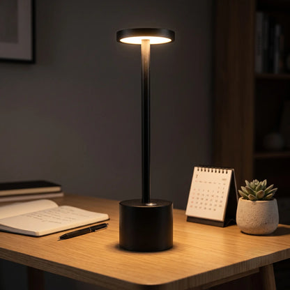 Aesthix Lume Halo black cordless dimmable table lamp glowing on a minimal study table with a book