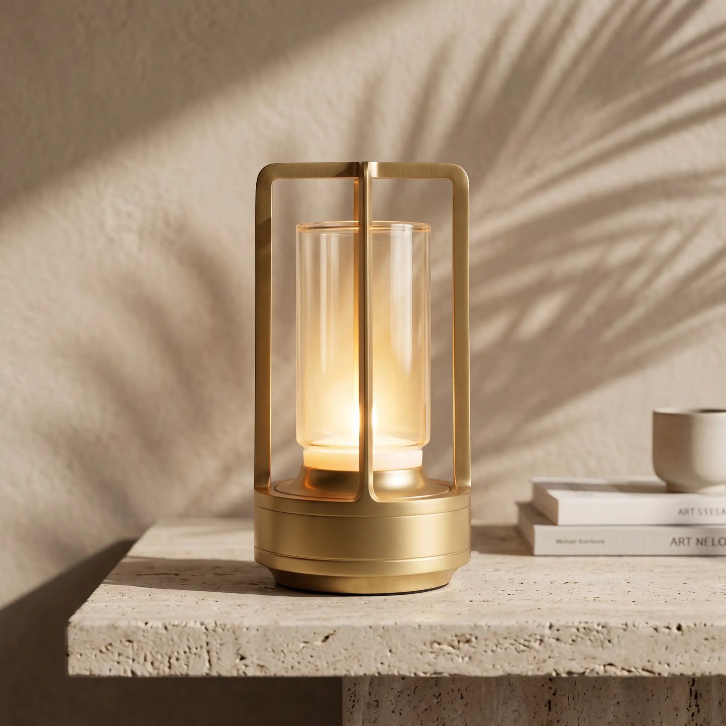Aesthix Lume Luxe gold glass lantern table lamp set on a textured stone surface with soft leaf shadows cast across a beige wall.