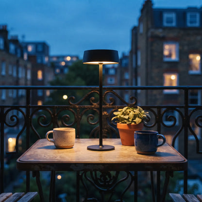 Aesthix Lume Plate white Nordic touch table lamp glowing on a balcony table at dusk