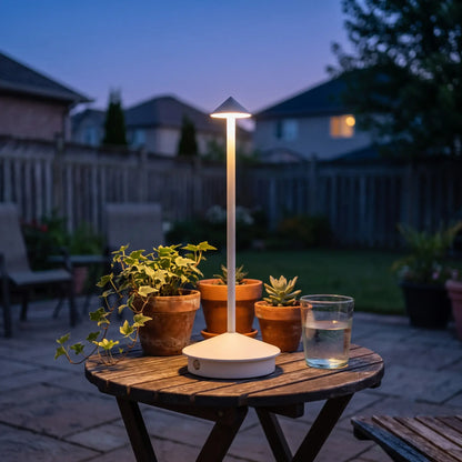 Aesthix Lume Vela slim rechargeable lamp glowing on an outdoor patio table with plants at dusk