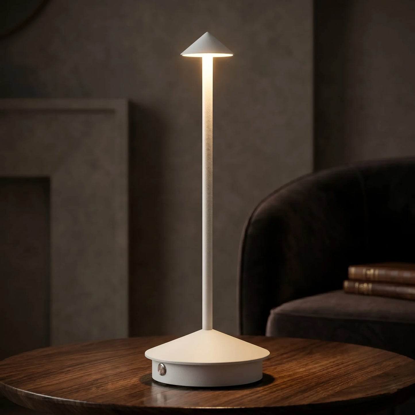 Aesthix Lume Vela slim rechargeable lamp glowing beside a cosy dark armchair