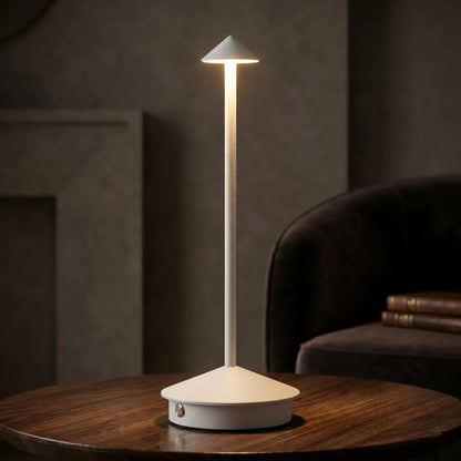 Aesthix Lume Vela slim rechargeable lamp glowing beside a cosy dark armchair