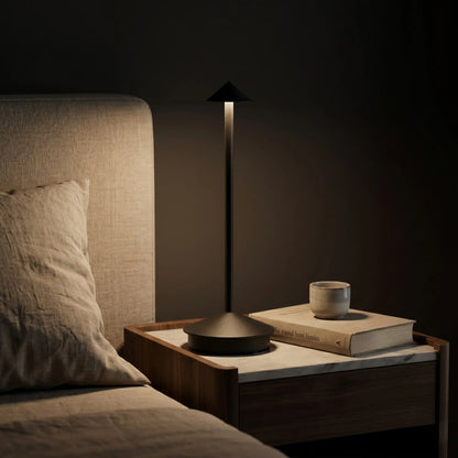 Aesthix Lume Vela slim rechargeable lamp glowing on a bedside table in a cosy dark bedroom