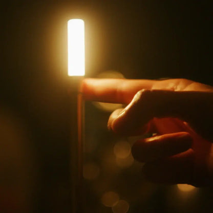 Aesthix Lume Taper Hand touching a lit candle against a dark background with a light source