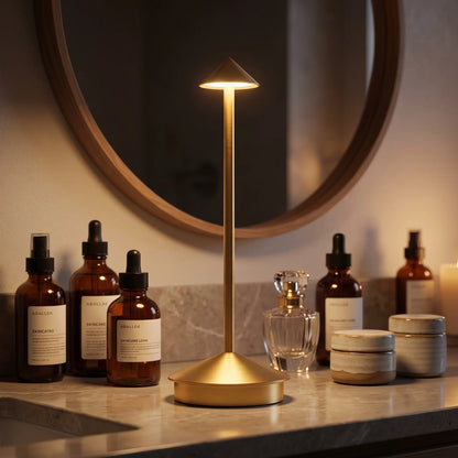 Aesthix Lume Vela slim rechargeable lamp on a vanity table beside amber glass bottles in a warmly lit bathroom settings