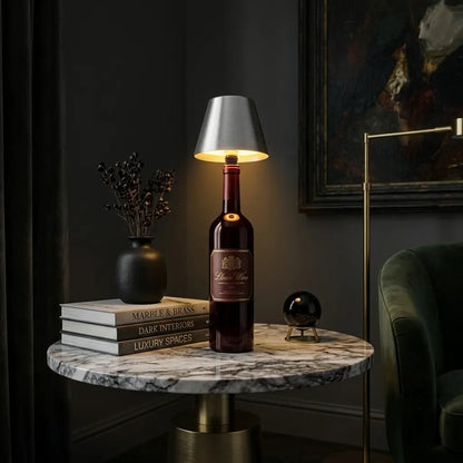 Aesthix Lume Vino, A wine bottle lamp with a silver conical shade and a glowing warm light inside, styled on a marble side table in a dark, elegant room.